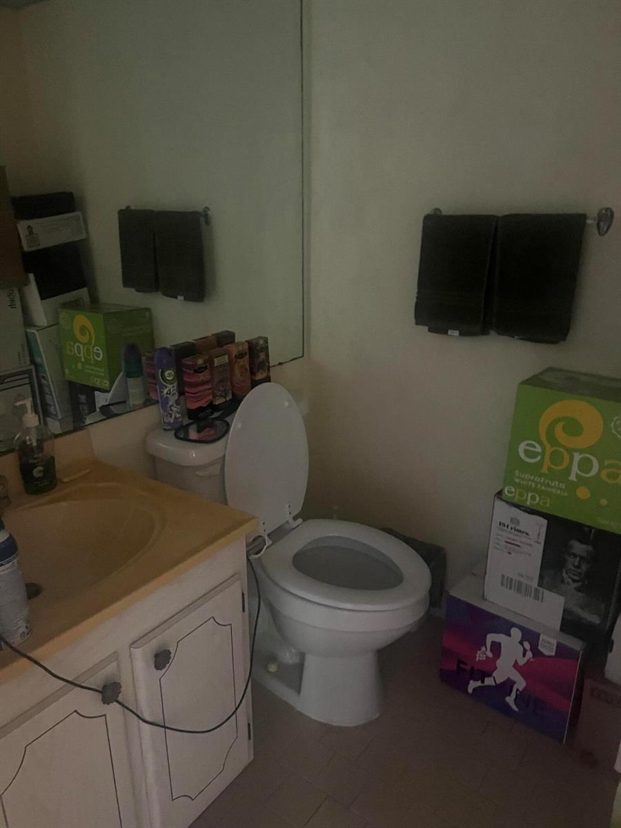A bathroom features a vanity with a sink, a toilet, and boxes stacked on the floor — 62 Valencia C, Delray Beach FL 33446, DELRAY BEACH, FL