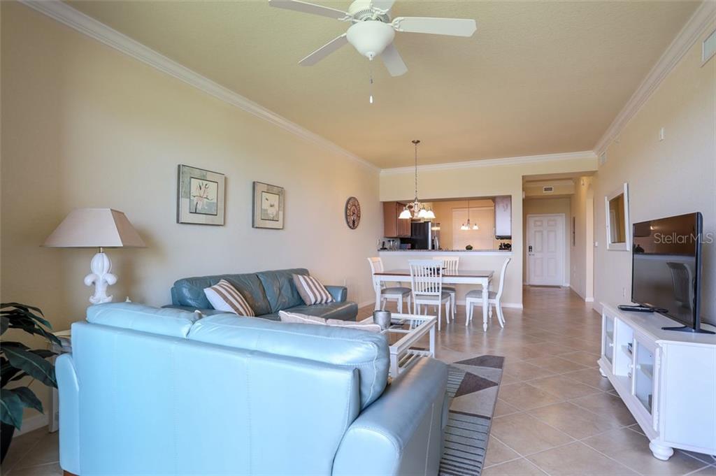 A living room and dining area with light blue sofas, tile floors, and a ceiling fan — 8309 GRAND ESTUARY TRAIL UNIT 204, BRADENTON, FL