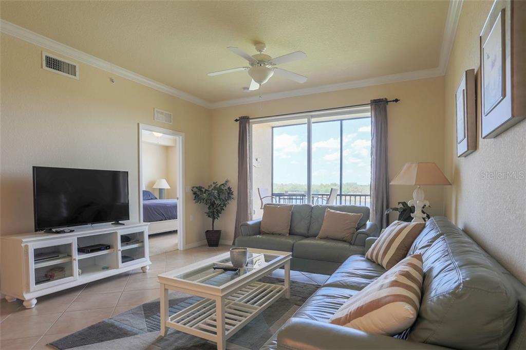 A living room with light tile floors, two leather sofas, a coffee table, and a balcony — 8309 GRAND ESTUARY TRAIL UNIT 204, BRADENTON, FL