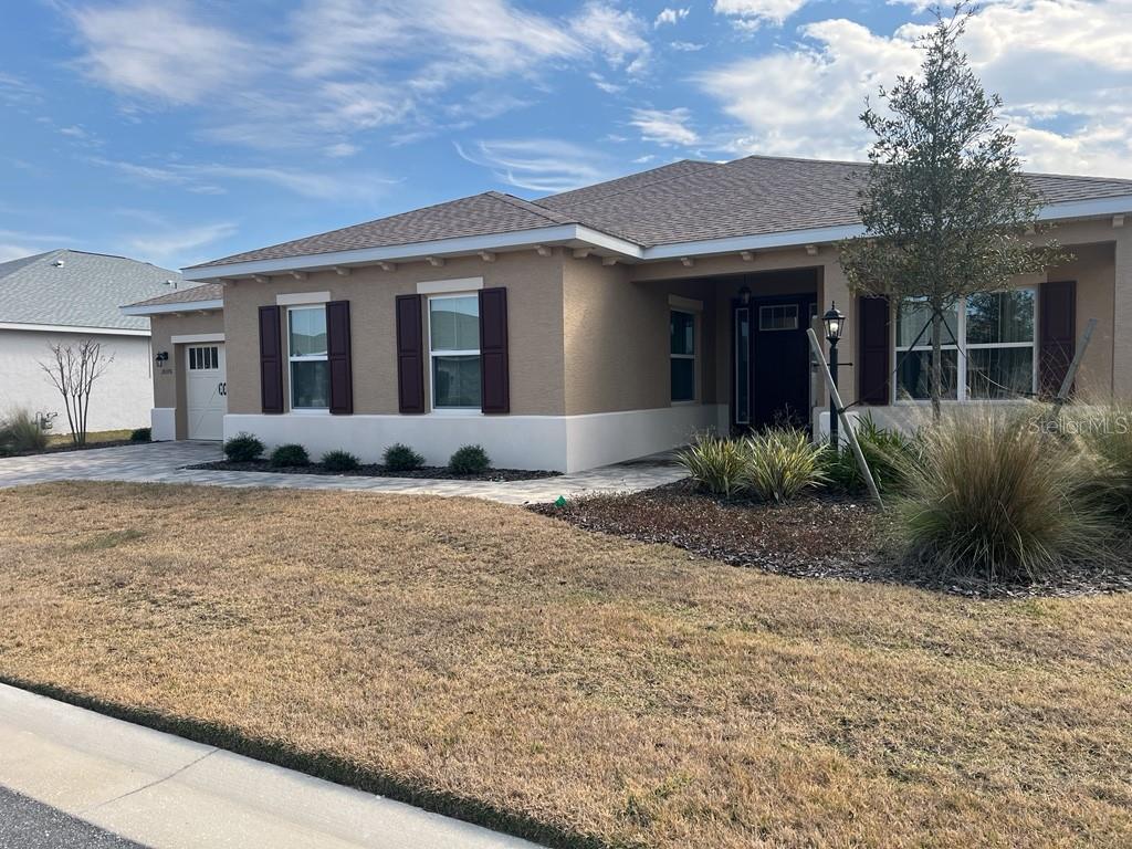 A tan single-story house with a brown roof, dark shutters, and a paved driveway — 10376 SW 99 STREET, OCALA, FL