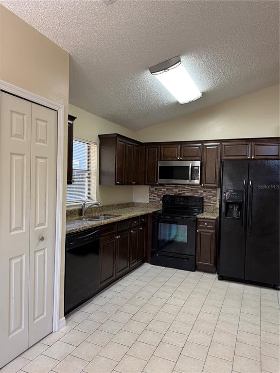 A kitchen features dark wood cabinets, black appliances, granite countertops, and light-colored tile flooring — 776 WOLF CREEK COURT, APOPKA, FL