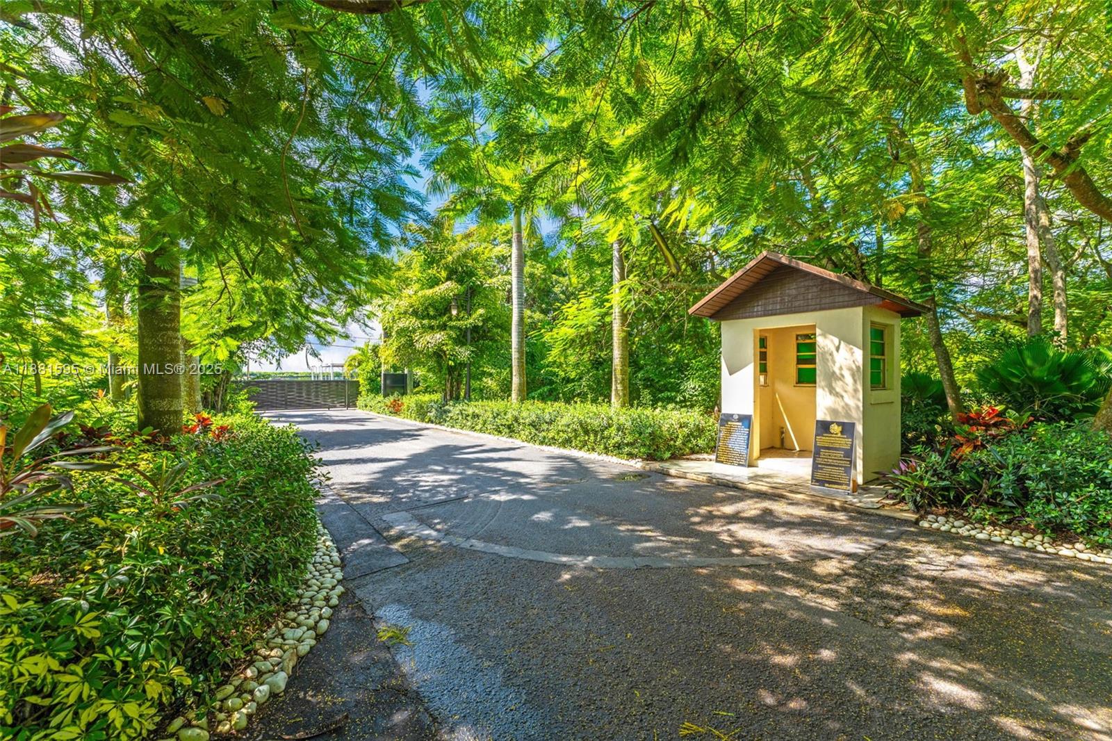 A paved driveway leads to a small guardhouse surrounded by lush trees and landscaping — 20701 SW 216th St, Miami FL 33170, MIAMI, FL