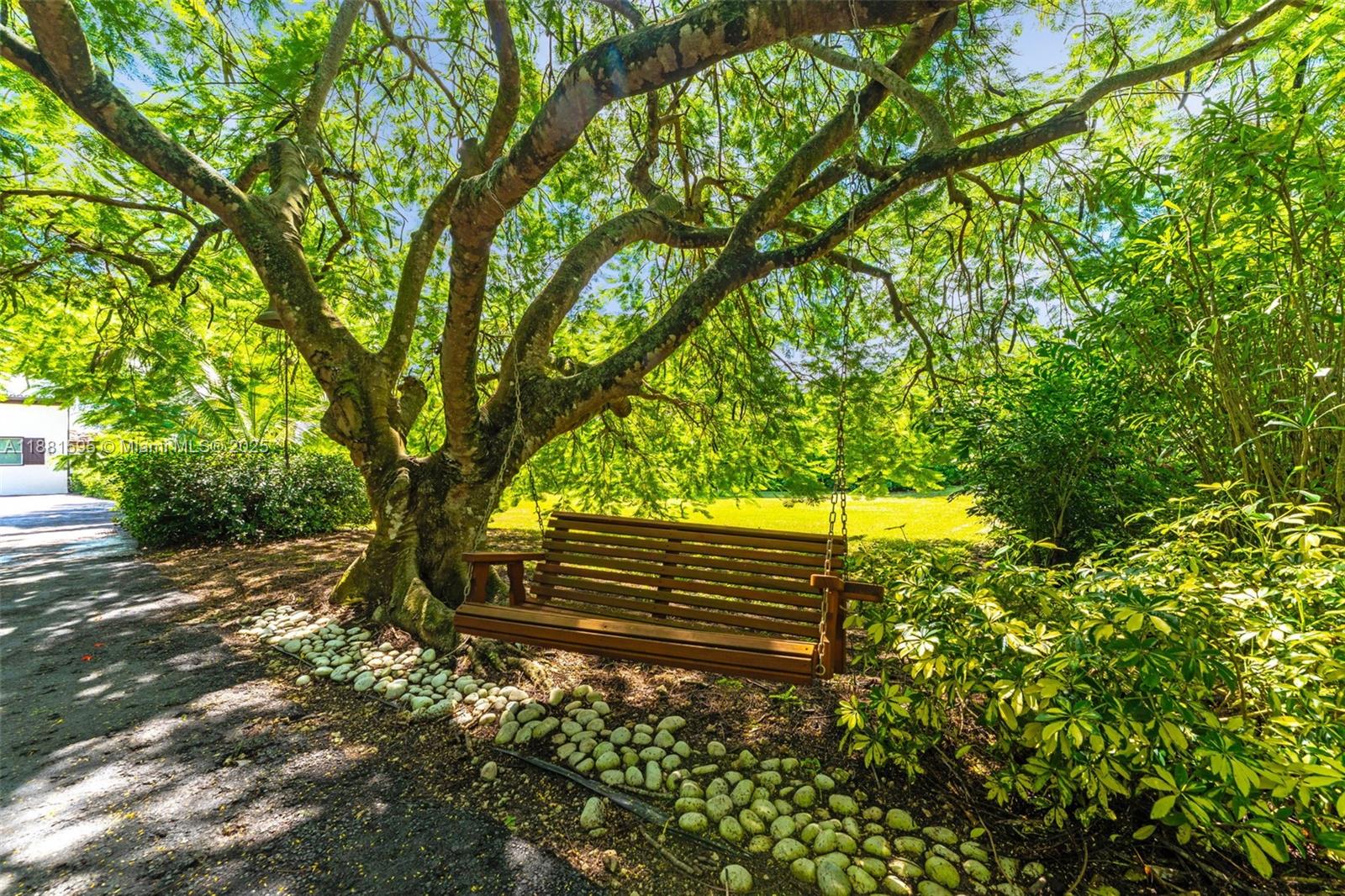 A wooden porch swing hangs from a large tree above a stone-lined garden path — 20701 SW 216th St, Miami FL 33170, MIAMI, FL