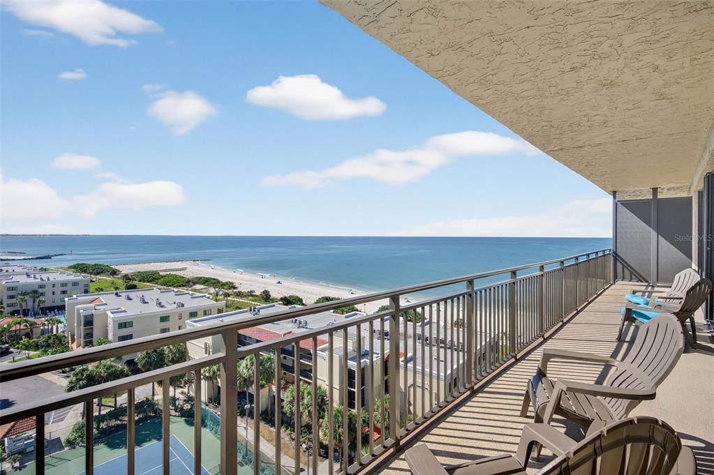 A balcony with chairs overlooks a beach, the ocean, and a tennis court below — 7600 BAYSHORE DRIVE UNIT 902, TREASURE ISLAND, FL