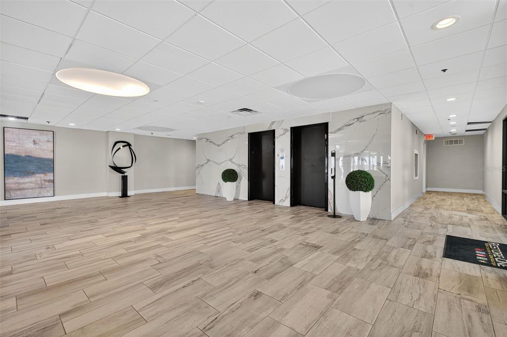A modern lobby features wood-look tile flooring, marble-accented elevator doors, and recessed ceiling lighting — 7600 BAYSHORE DRIVE UNIT 902, TREASURE ISLAND, FL