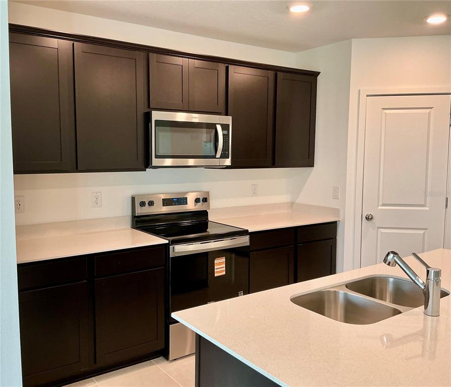 A kitchen features dark wood cabinets, stainless steel appliances, and a white quartz island countertop — 3786 BENHAM RISE ROAD, SPRING HILL, FL