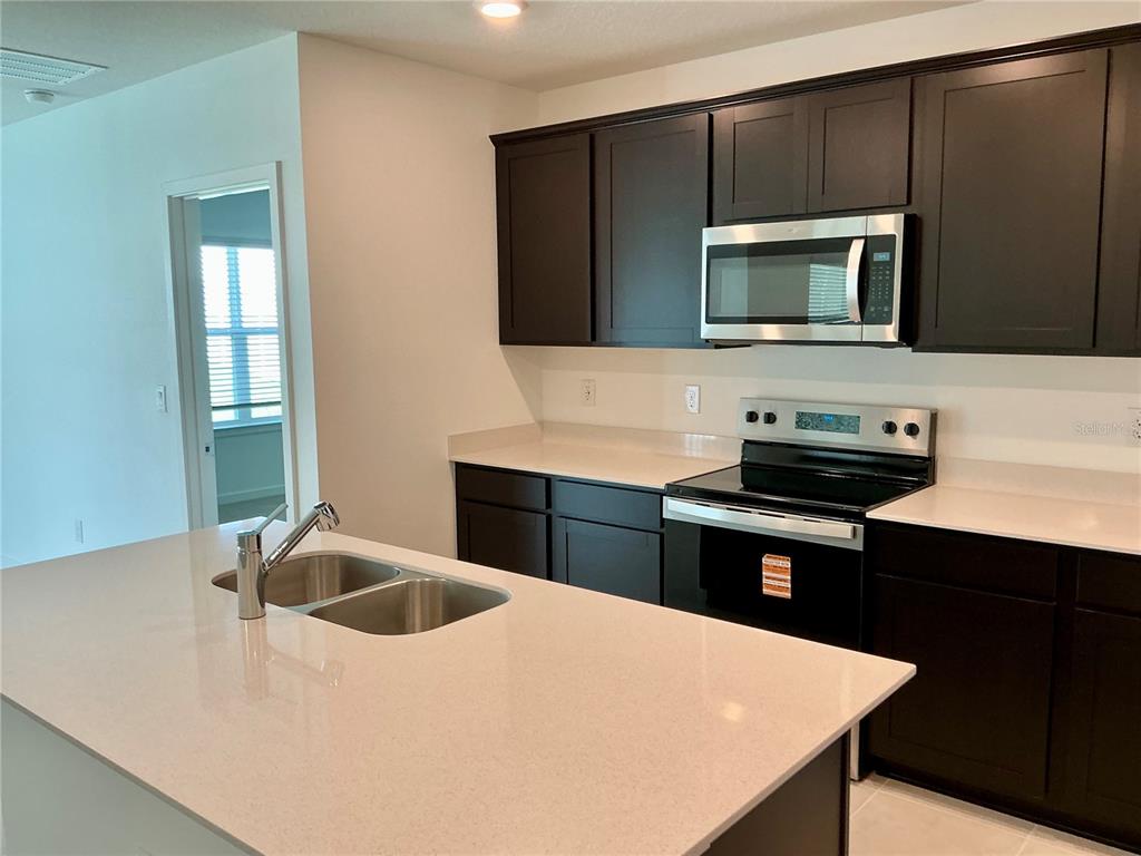 A kitchen with dark cabinets, white countertops, a stainless steel microwave, and a center island — 3786 BENHAM RISE ROAD, SPRING HILL, FL