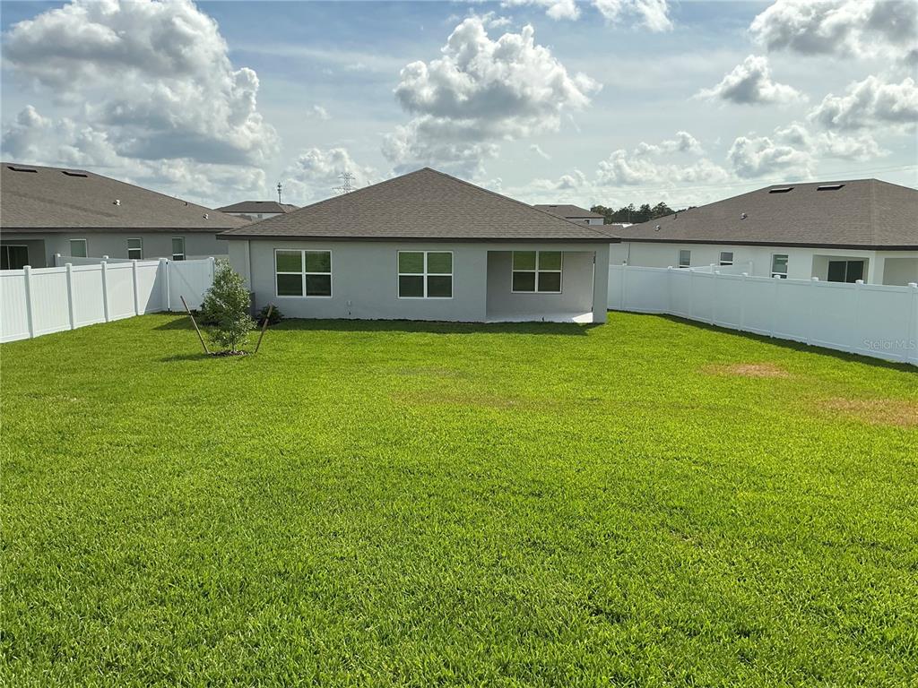 The rear exterior of a single-story house features a covered patio and a fenced yard — 3786 BENHAM RISE ROAD, SPRING HILL, FL