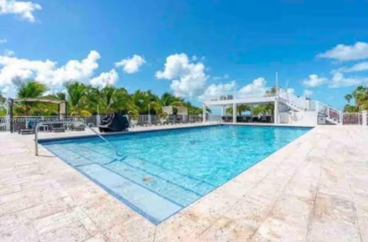 A rectangular swimming pool with steps is surrounded by a stone patio and palm trees — 325 Calusa St #5, Key Largo FL 33037, KEY LARGO, FL