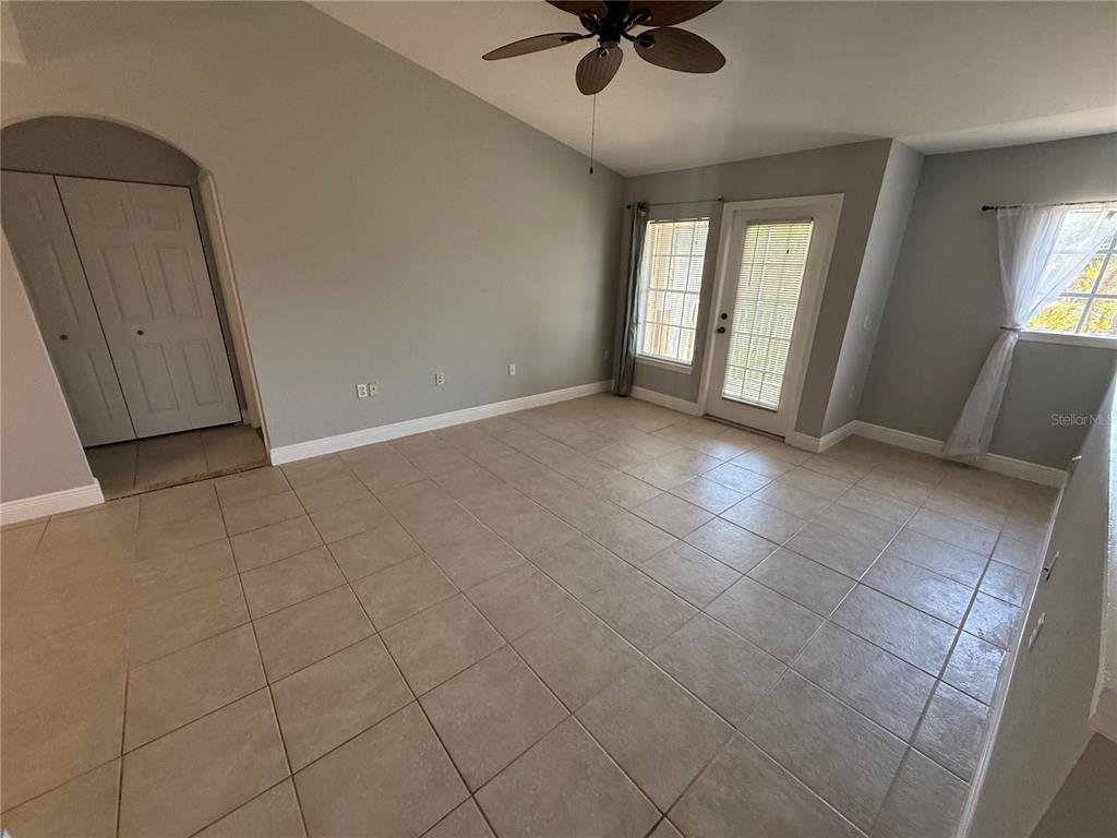 An empty room with light-colored tile flooring, gray walls, a ceiling fan, and glass doors — 8932 MANOR LOOP UNIT 205, LAKEWOOD RANCH, FL