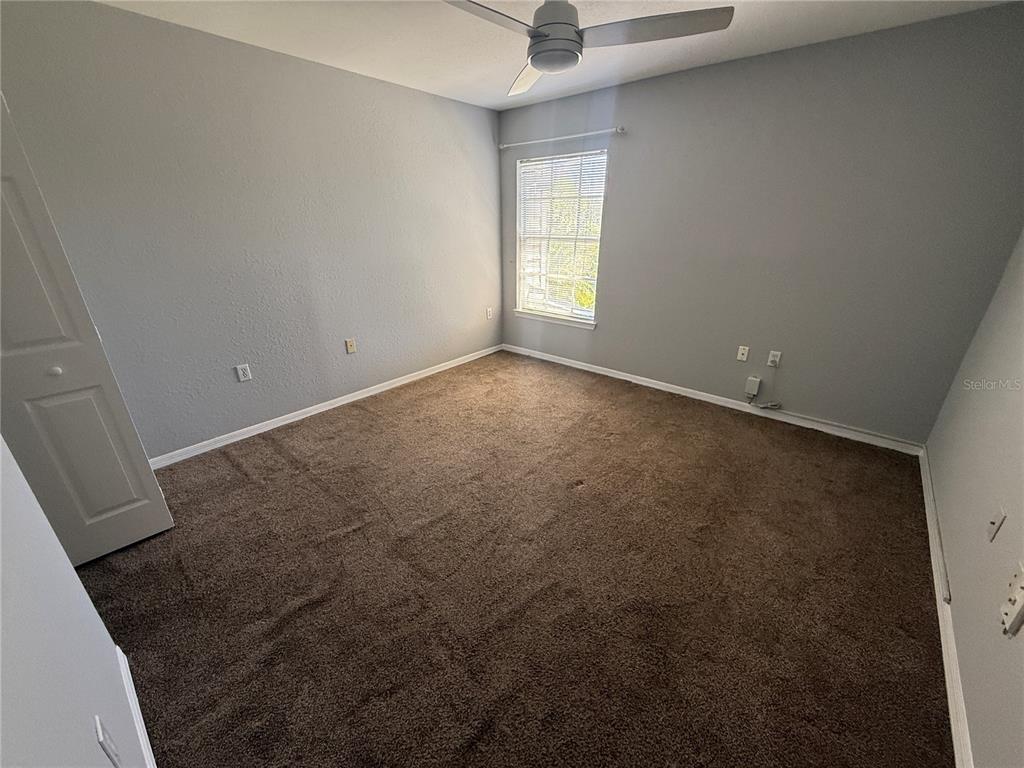 An empty bedroom features gray walls, brown carpeting, a ceiling fan, and a single window — 8932 MANOR LOOP UNIT 205, LAKEWOOD RANCH, FL