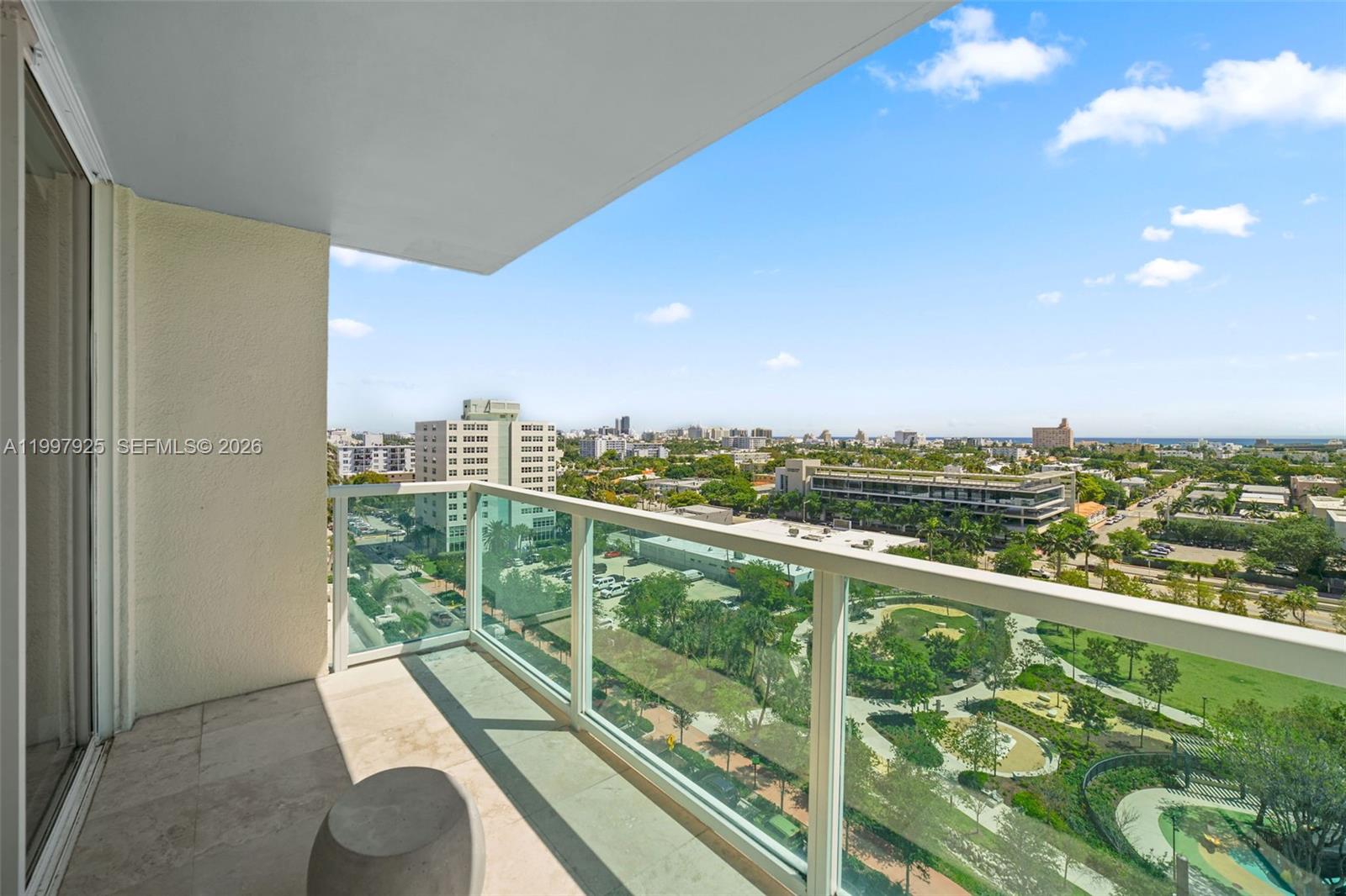 A high-rise balcony with a glass railing overlooks a park and city skyline — 650 West Ave # 1104, Miami Beach FL 33139, MIAMI BEACH, FL