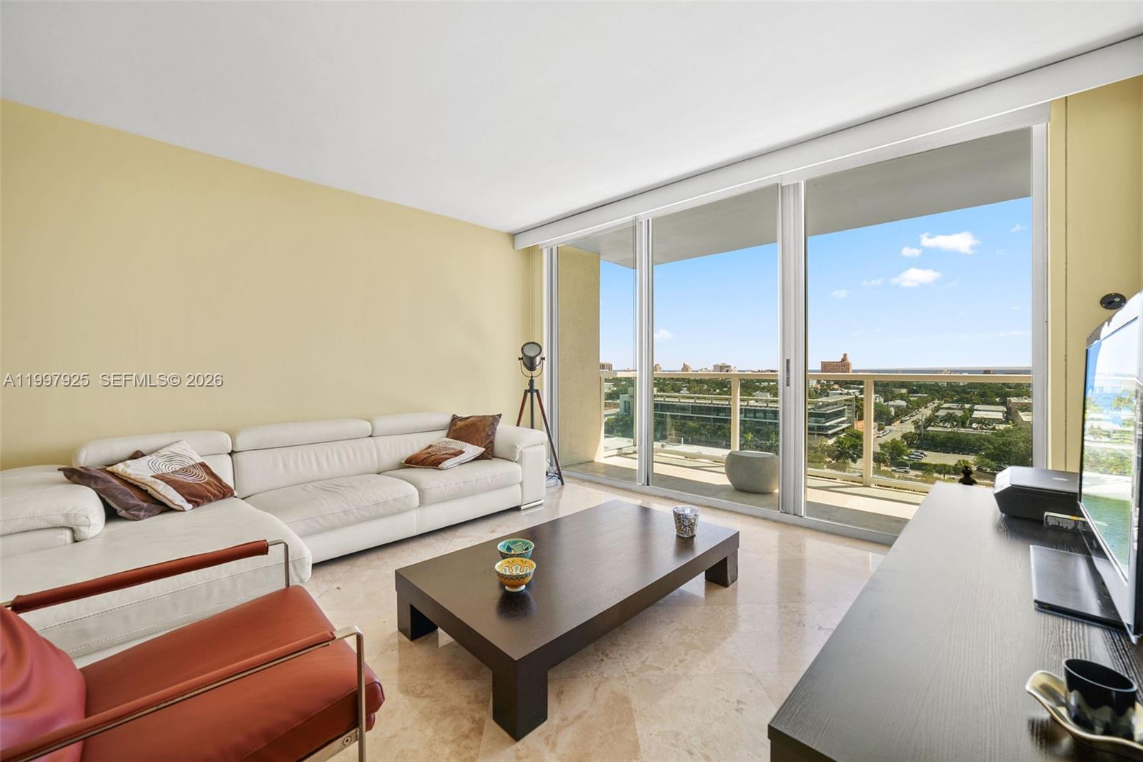 A living room with a white sectional sofa, dark coffee table, and floor-to-ceiling balcony doors — 650 West Ave # 1104, Miami Beach FL 33139, MIAMI BEACH, FL