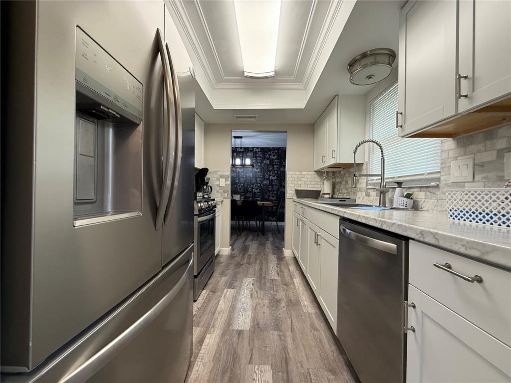 A galley kitchen features stainless steel appliances, white cabinetry, and light-colored countertops — 3988 SAN LUIS DRIVE, SARASOTA, FL