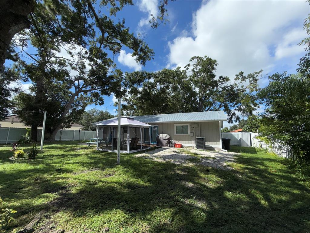 A backyard features a house with a metal roof, a screened gazebo, and mature trees — 3988 SAN LUIS DRIVE, SARASOTA, FL