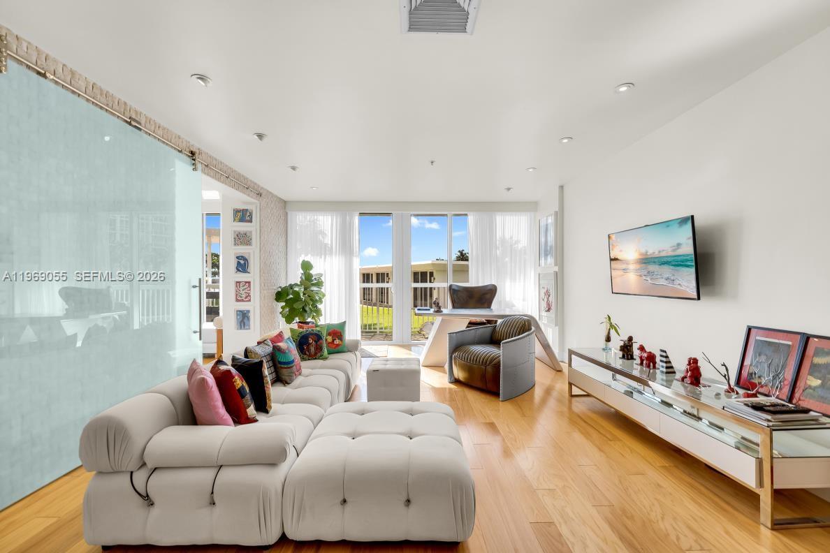A modern living room features a white sectional sofa, hardwood floors, and a wall-mounted television — 10275 Collins Ave # 102, Bal Harbour FL 33154, BAL HARBOUR, FL