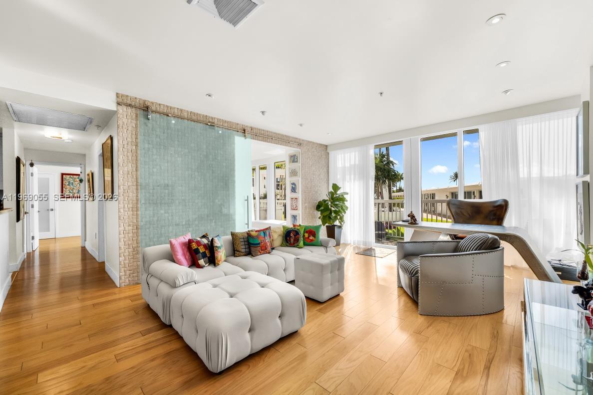 A living room features a white tufted sectional, a glass sliding door, and hardwood floors — 10275 Collins Ave # 102, Bal Harbour FL 33154, BAL HARBOUR, FL