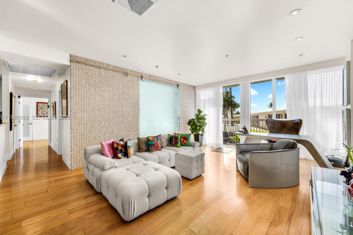 A living room features a tufted sectional sofa, a desk, and a textured stone accent wall — 10275 Collins Ave # 102, Bal Harbour FL 33154, BAL HARBOUR, FL