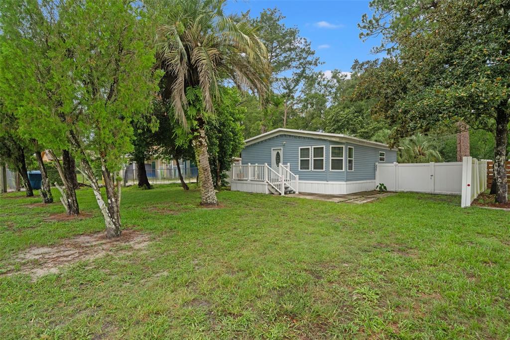 A blue mobile home with a white deck sits on a grassy lot with trees — 237 MONROE AVENUE, BROOKSVILLE, FL