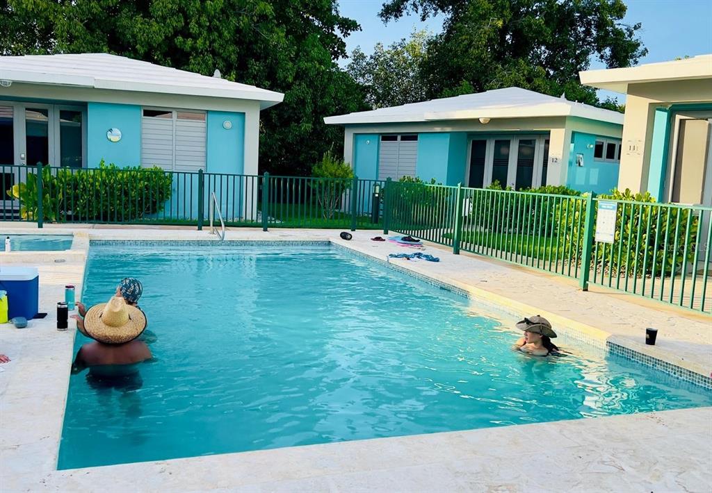 Two people swim in a rectangular outdoor pool in front of blue vacation cottages — 3418 CALLE UROYUAN, RINCON, PR