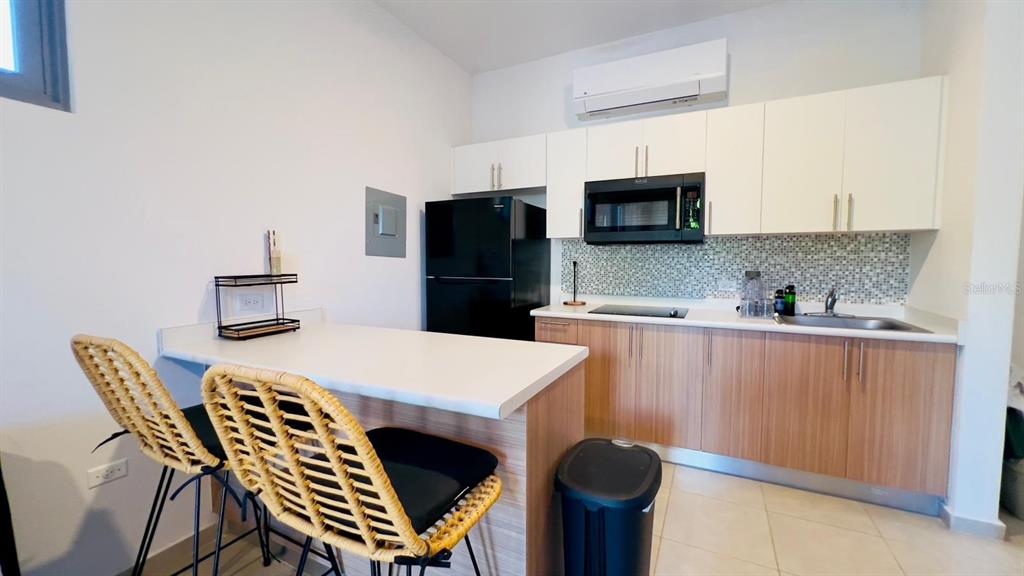 A kitchen features light wood cabinets, white upper cabinets, a black refrigerator, and a breakfast bar — 3418 CALLE UROYUAN, RINCON, PR