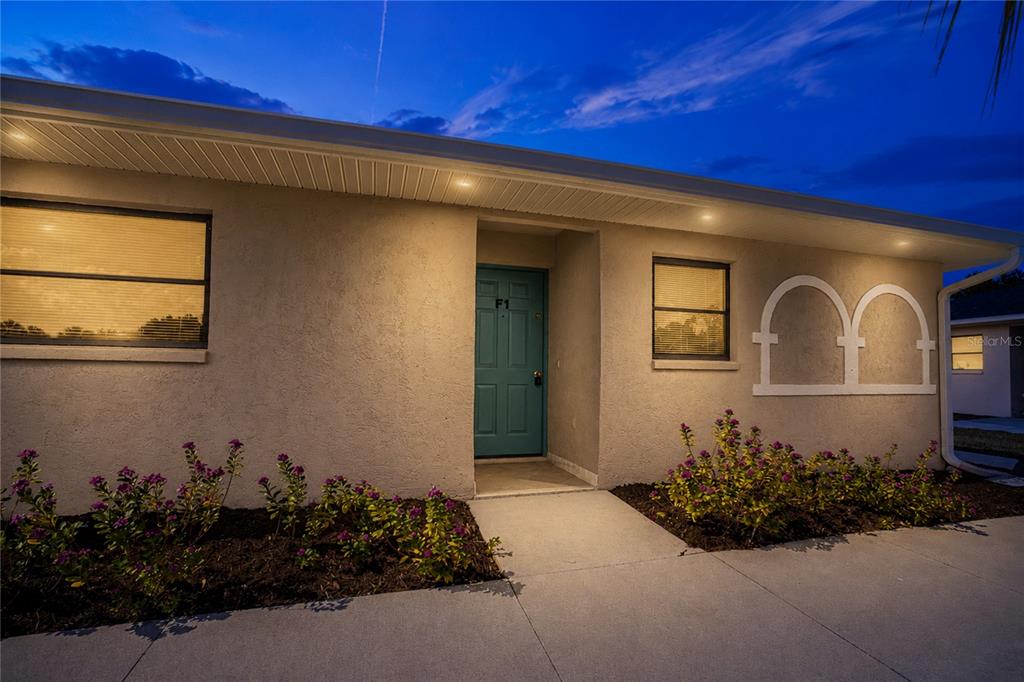 The exterior of a single-story building features a teal front door and landscaped flower beds — 24540 HARBORVIEW ROAD UNIT F1, PUNTA GORDA, FL