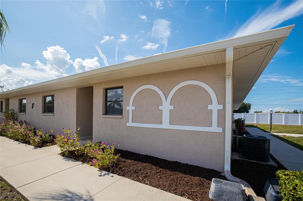 The exterior of a tan stucco building features a decorative white arch wall detail — 24540 HARBORVIEW ROAD UNIT F1, PUNTA GORDA, FL