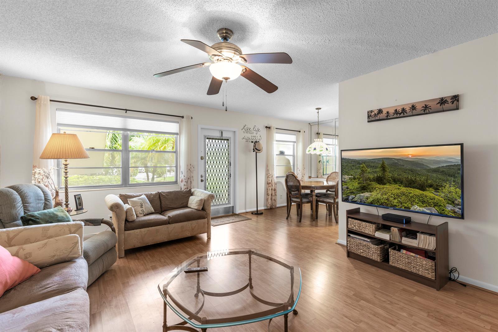 A living room with wood-look flooring, a ceiling fan, a television, and a dining area — 266 Ventnor S, Deerfield Beach FL 33442, DEERFIELD BEACH, FL