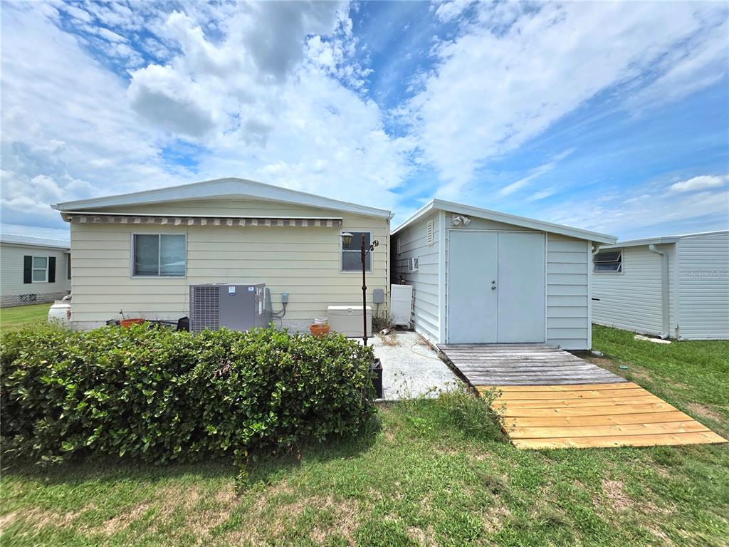 The exterior of a mobile home features a shed, a wooden ramp, and a bush — 5334 COMANCHE STREET, ZEPHYRHILLS, FL