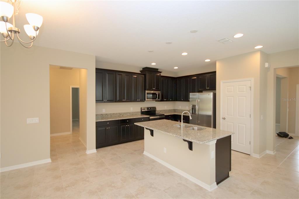 A kitchen features dark wood cabinets, granite countertops, a center island, and stainless steel appliances — 11415 ACACIA GROVE LANE, RIVERVIEW, FL
