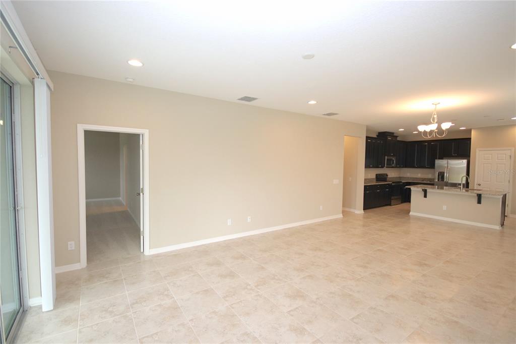 An open-concept living area features light tile flooring, beige walls, and an adjacent dark-cabinet kitchen — 11415 ACACIA GROVE LANE, RIVERVIEW, FL
