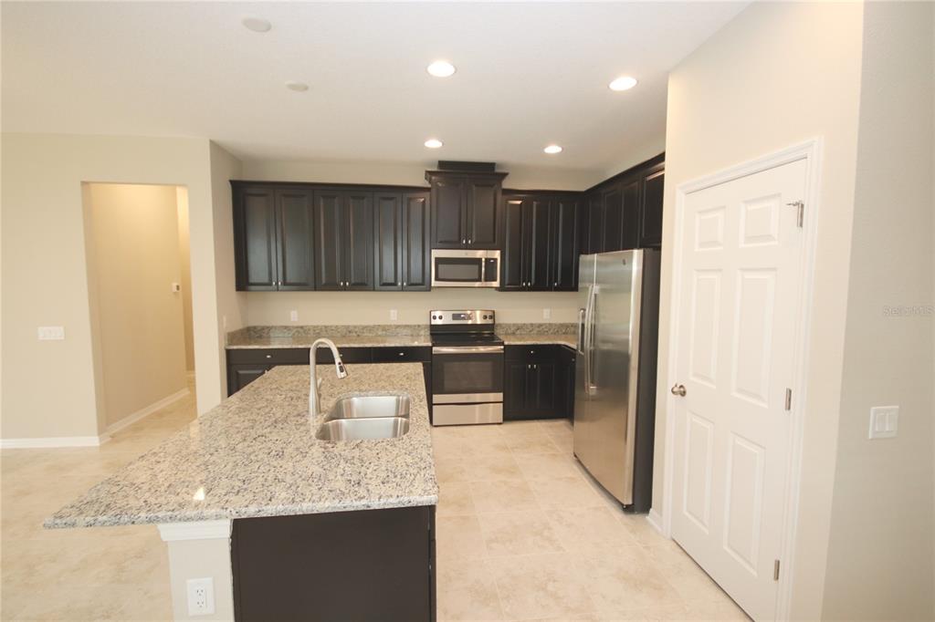 A kitchen features dark wood cabinets, granite countertops, stainless steel appliances, and a central island — 11415 ACACIA GROVE LANE, RIVERVIEW, FL