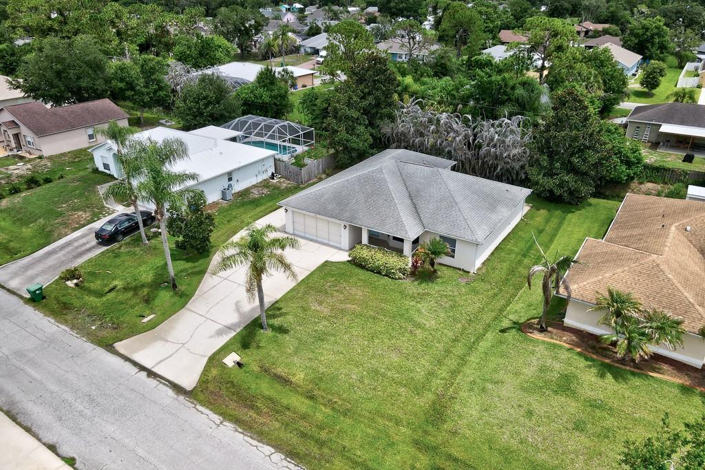 An aerial view shows a suburban house with a gray roof, driveway, and palm trees — SEBASTIAN, FL