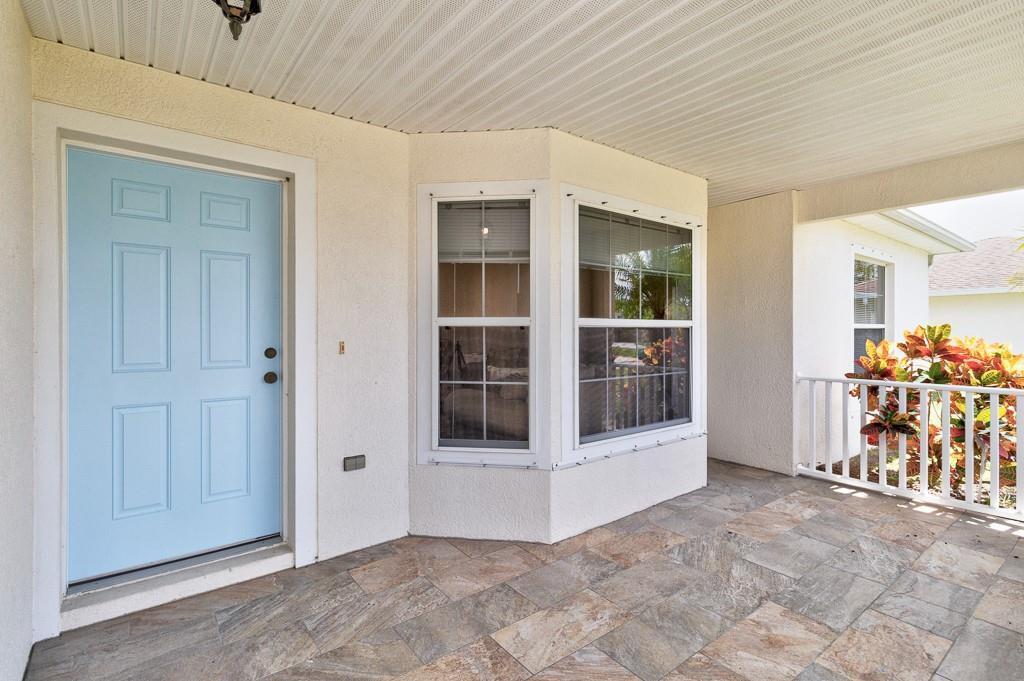 A covered porch features a light blue front door, bay windows, and tiled flooring — SEBASTIAN, FL