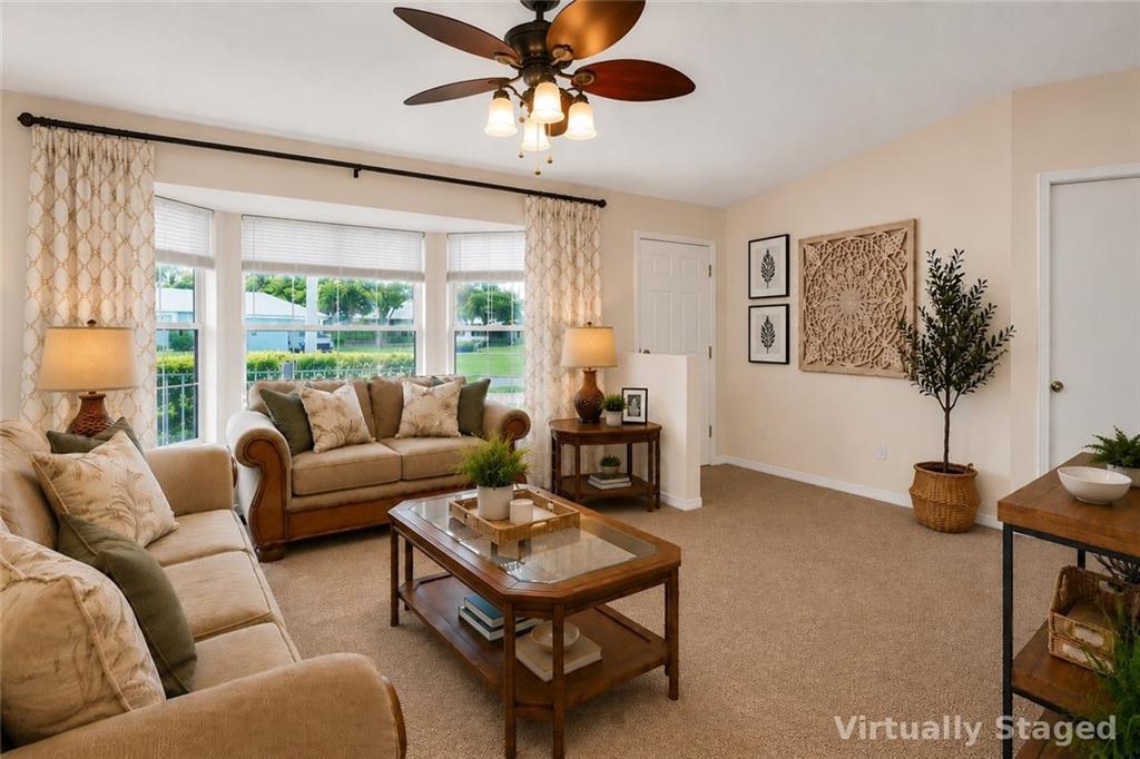 A living room with beige carpet, a ceiling fan, and a bay window with curtains — SEBASTIAN, FL