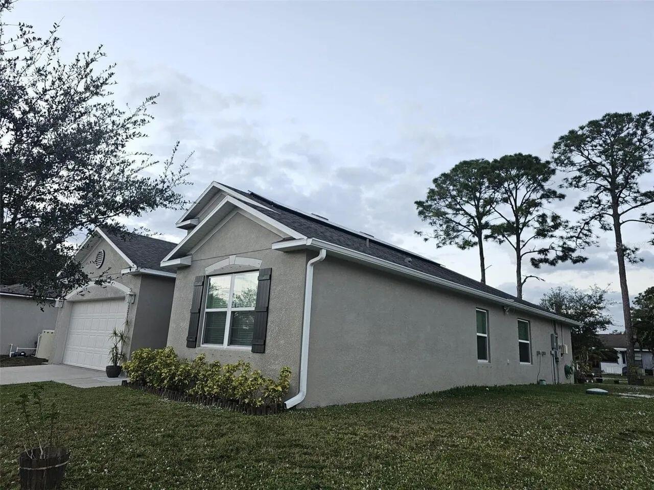 A single-story house with a gray stucco exterior, a two-car garage, and a lawn — 1357 Sequoia Road NW, Palm Bay FL 32907, PALM BAY, FL
