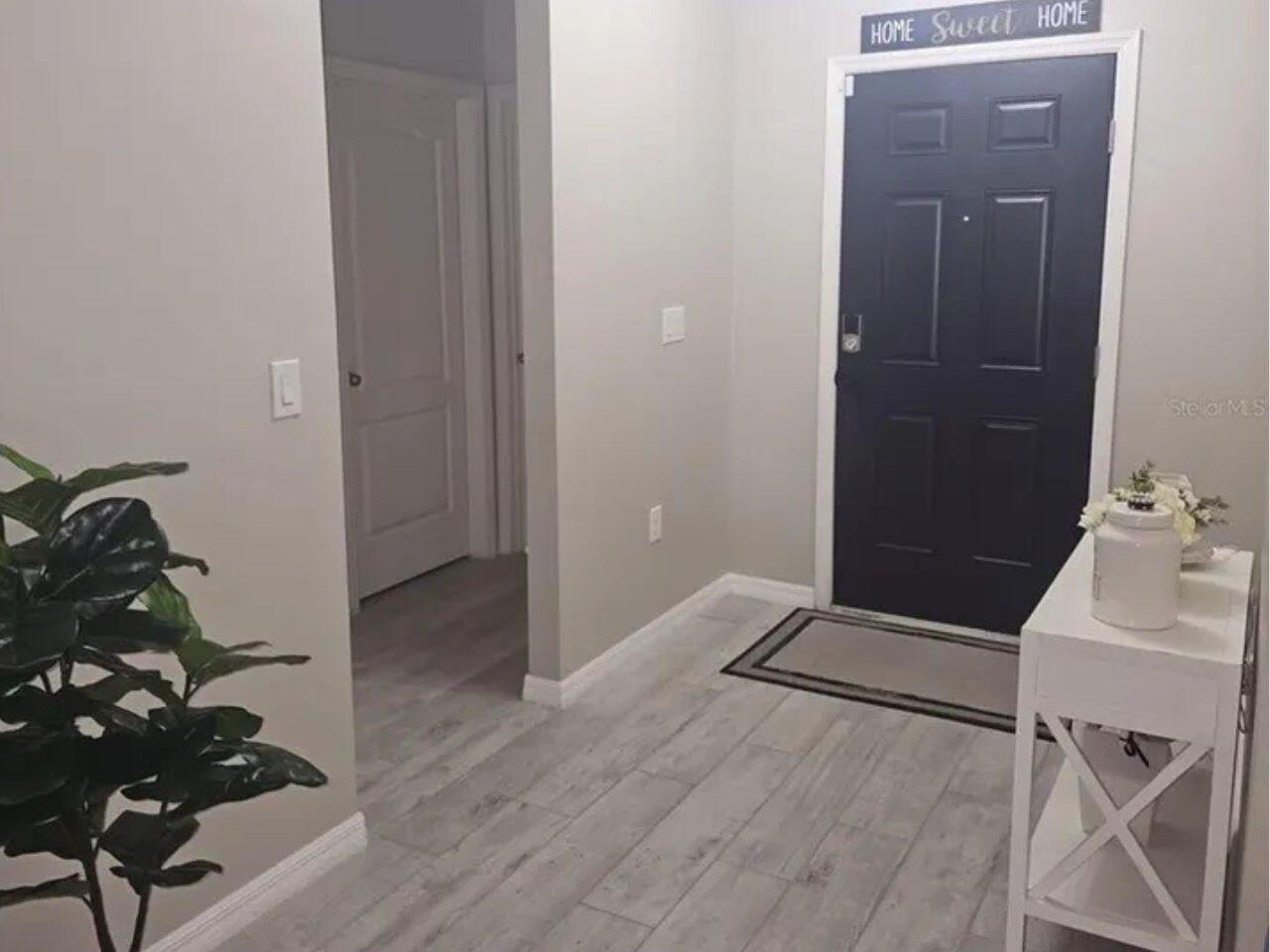 An entryway features light wood-look flooring, a dark front door, and a white console table — 1357 Sequoia Road NW, Palm Bay FL 32907, PALM BAY, FL