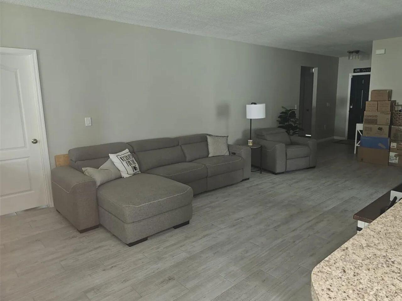A living room features a gray sectional sofa, matching armchair, and light wood-look tile flooring — 1357 Sequoia Road NW, Palm Bay FL 32907, PALM BAY, FL