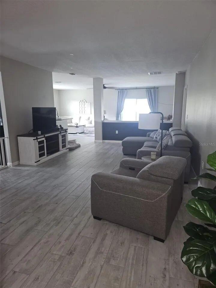 A living room features gray wood-look tile flooring, a sectional sofa, and a television console — 1357 Sequoia Road NW, Palm Bay FL 32907, PALM BAY, FL