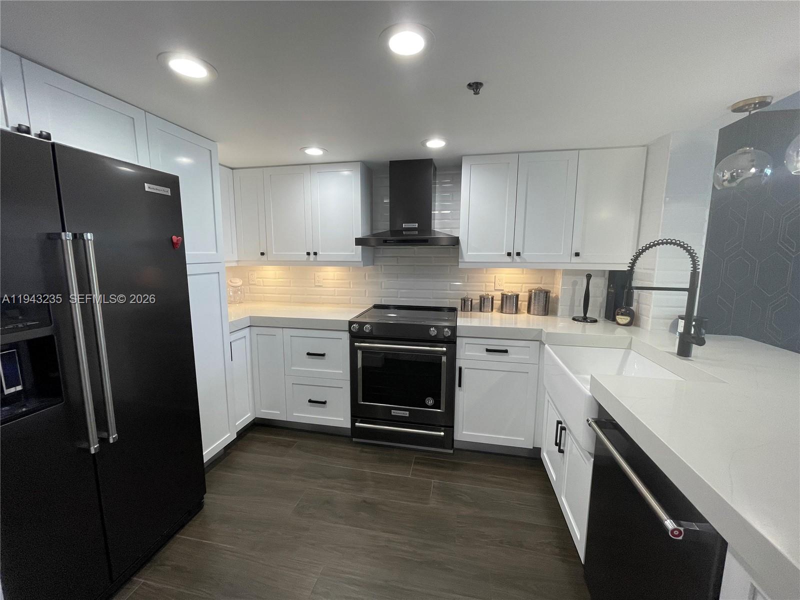 A modern kitchen features white cabinets, black appliances, a farmhouse sink, and dark wood flooring — 2555 Collins Ave # 1409, Miami Beach FL 33140, MIAMI BEACH, FL