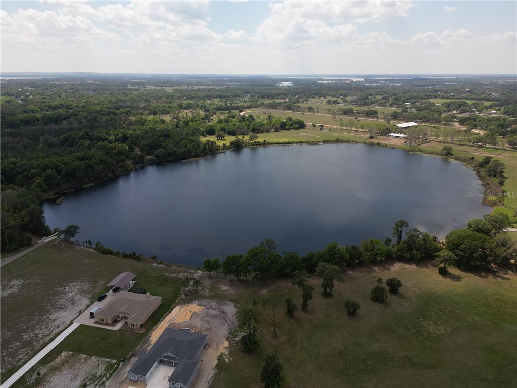 An aerial view shows a large lake surrounded by green fields, trees, and two houses — 3430 LAKE DIANE ROAD, TAVARES, FL