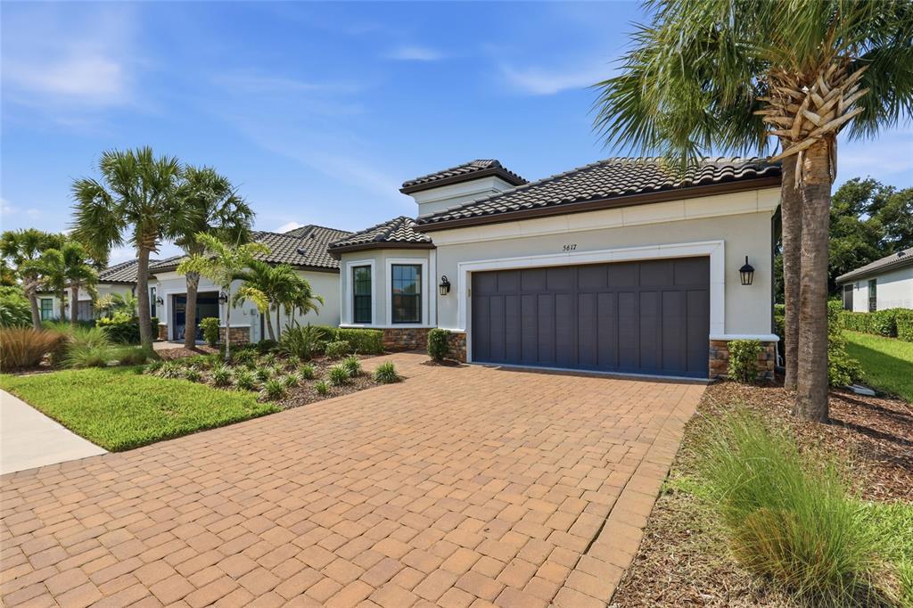 A single-story house with a paved driveway, a dark garage door, and palm trees — 5617 SCARLOTTI STREET, NOKOMIS, FL