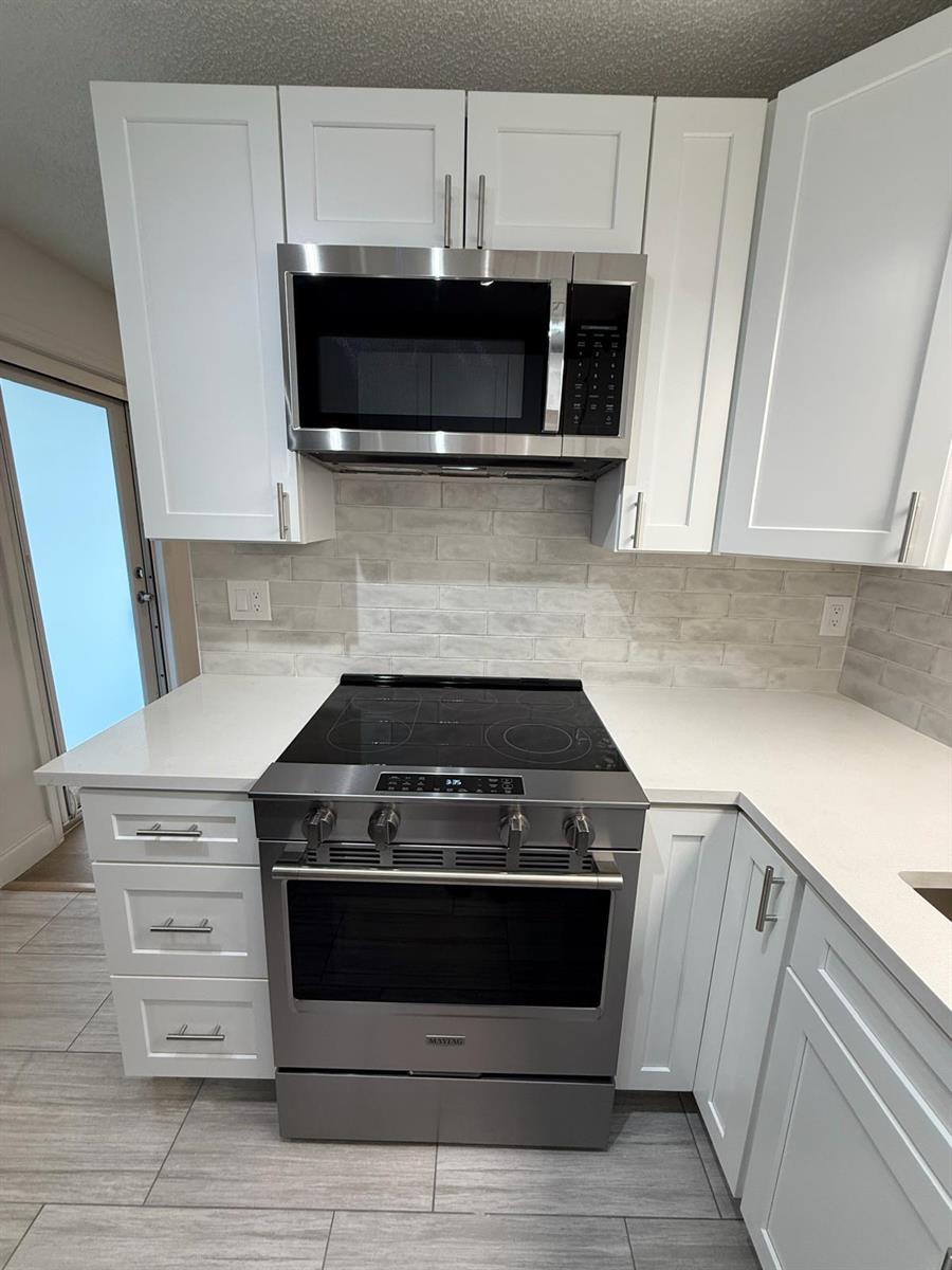 A kitchen features white cabinets, stainless steel appliances, a glass-top stove, and a tiled backsplash — 2630 W 28th Street, Riviera Beach FL 33404, RIVIERA BEACH, FL