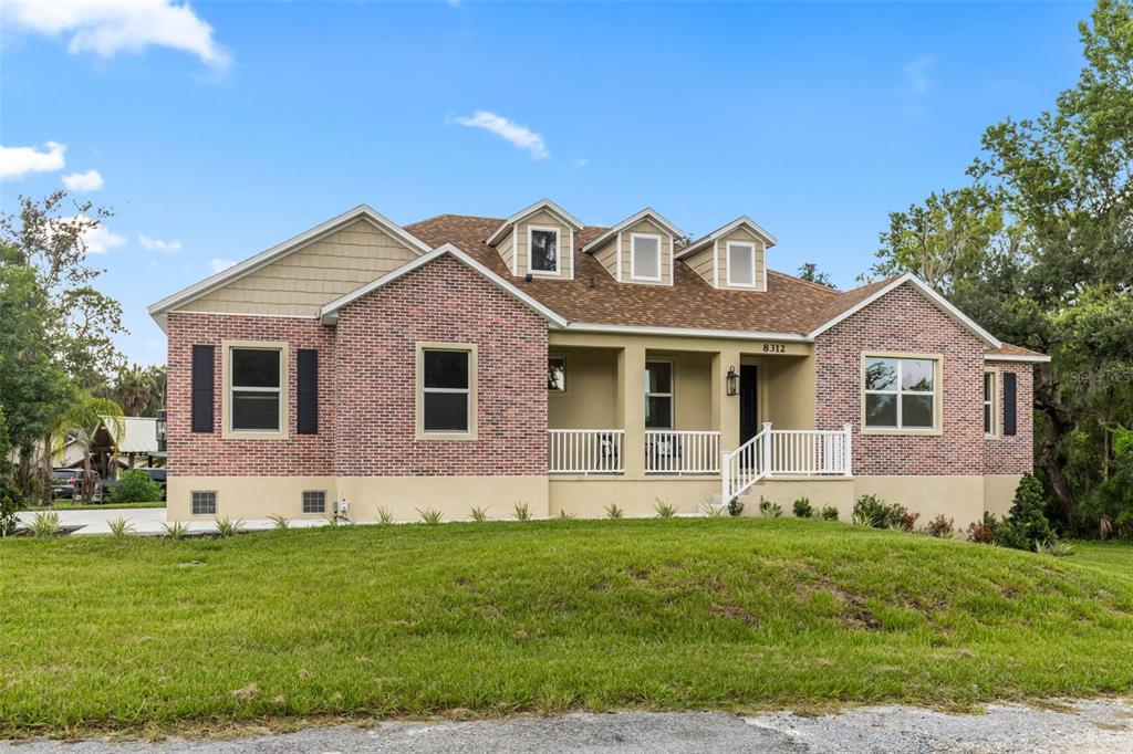 A brick house with a front porch and three dormer windows under a sunset sky — 8312 REVELS ROAD, RIVERVIEW, FL