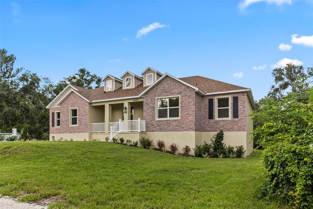 An exterior view of a single-story brick house with a covered porch and dormer windows — 8312 REVELS ROAD, RIVERVIEW, FL