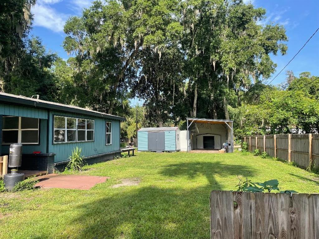A backyard features a teal house, a small storage shed, and a covered outdoor structure — 430 SE 74TH STREET, GAINESVILLE, FL