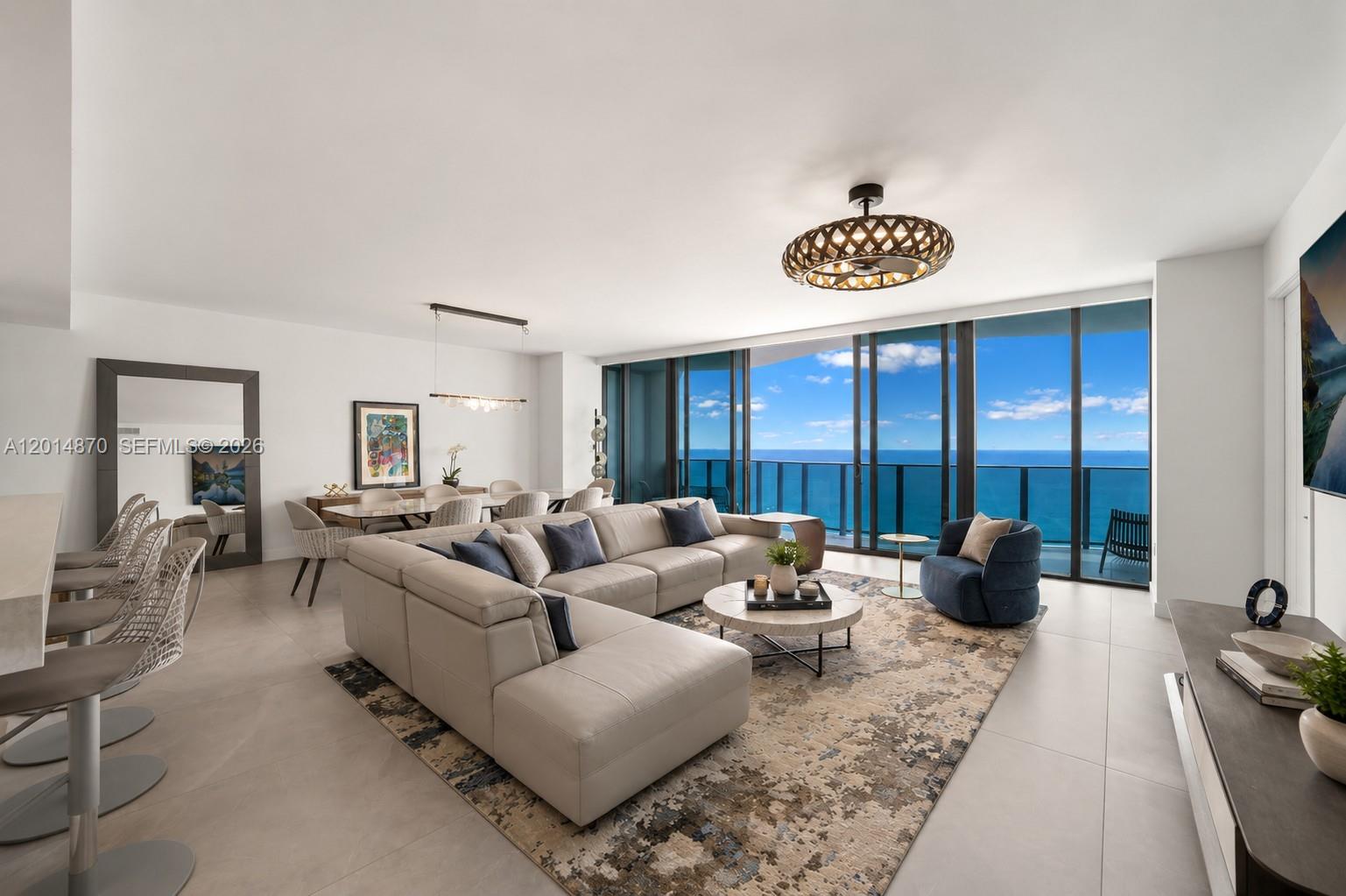 A modern living room features a large sectional sofa, dining area, and floor-to-ceiling ocean views — 900 N Ocean Blvd # 1903, Pompano Beach FL 33062, POMPANO BEACH, FL