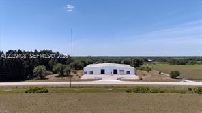 A white metal warehouse building stands in a rural field under a clear blue sky — 14961 W State Road 78, Moore Haven FL 33471, MOORE HAVEN, FL