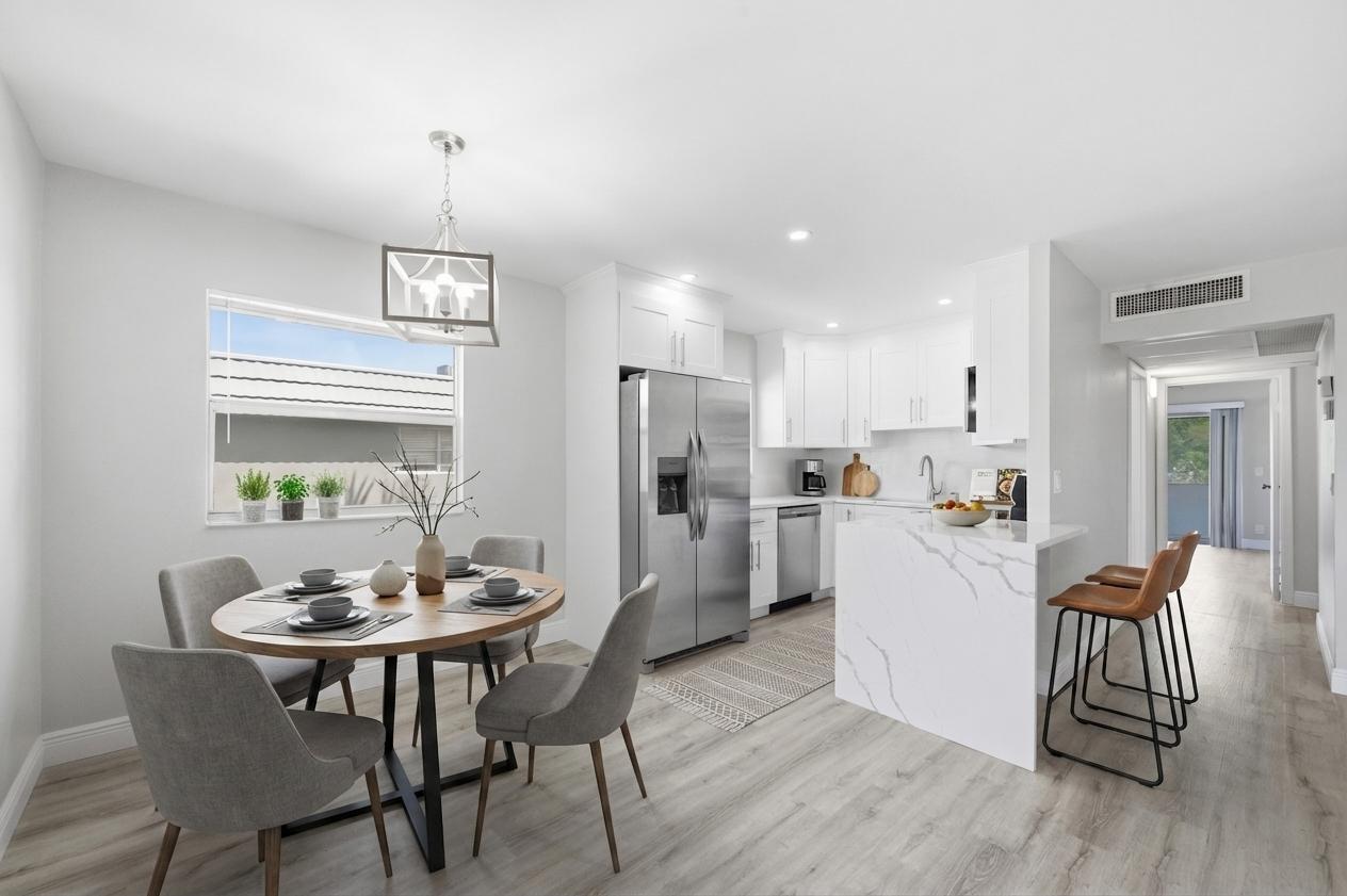A bright kitchen and dining area features white cabinetry, marble-look countertops, and light wood flooring — 284 Flanders F, Delray Beach FL 33484, DELRAY BEACH, FL
