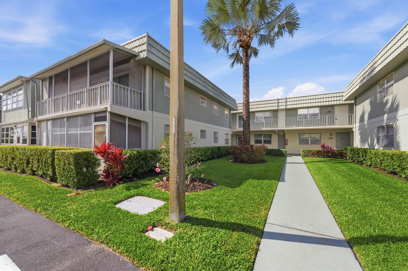 A two-story apartment building with a central walkway, green lawn, and a palm tree — 284 Flanders F, Delray Beach FL 33484, DELRAY BEACH, FL